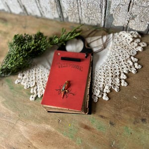 May include: A red telephone address book with a black metal backing and a hanging loop. The front cover features the word TELEPHONE in black text and a small, colorful parrot figurine perched on a branch illustration in the center.
