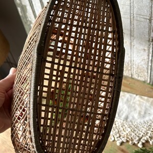 May include: A woven brown wicker basket with an oval shape. The basket has a dark brown trim around the top edge. The interior of the basket is visible through the woven pattern.