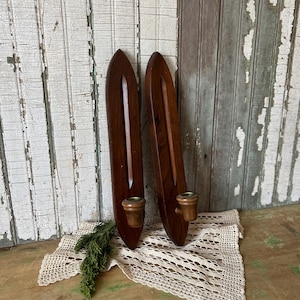 May include: Two vintage wooden wall sconces with a dark brown finish. Each sconce features a candle holder. The sconces are displayed on a white lace doily with a sprig of greenery.