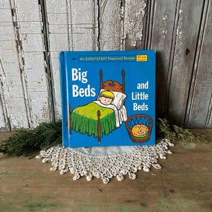 May include: A vintage children's book titled "Big Beds and Little Beds" with a blue cover. The cover illustration depicts a child in a bed and a cat in a basket. The book is an Early-Start Preschool Reader.