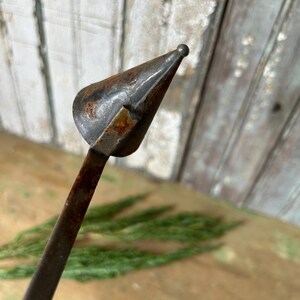 May include: Close-up of a vintage metal tool with a conical head and a long, slender handle. The tool has a rusty, aged appearance, suggesting it's an antique. The head has a small, rounded tip.