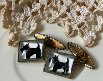 May include: A pair of gold cufflinks with a black and white image of a Scottish terrier dog inside a clear glass frame.