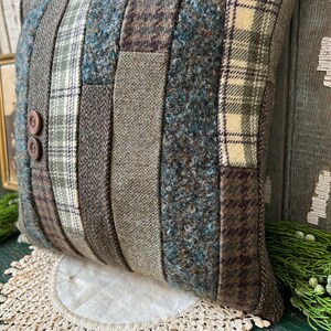 K&ouml;nnte beinhalten: Ein braunes und gr&uuml;nes Patchwork-Kissen mit Knopfdetail. Das Kissen liegt auf einer wei&szlig;en H&auml;kelspitze.
