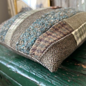 K&ouml;nnte beinhalten: Ein braunes, gr&uuml;nes und blaues Patchwork-Kissen mit Knopfdetail. Das Kissen ist aus einem weichen, strukturierten Stoff gefertigt und hat einen leicht ausgefransten Rand.