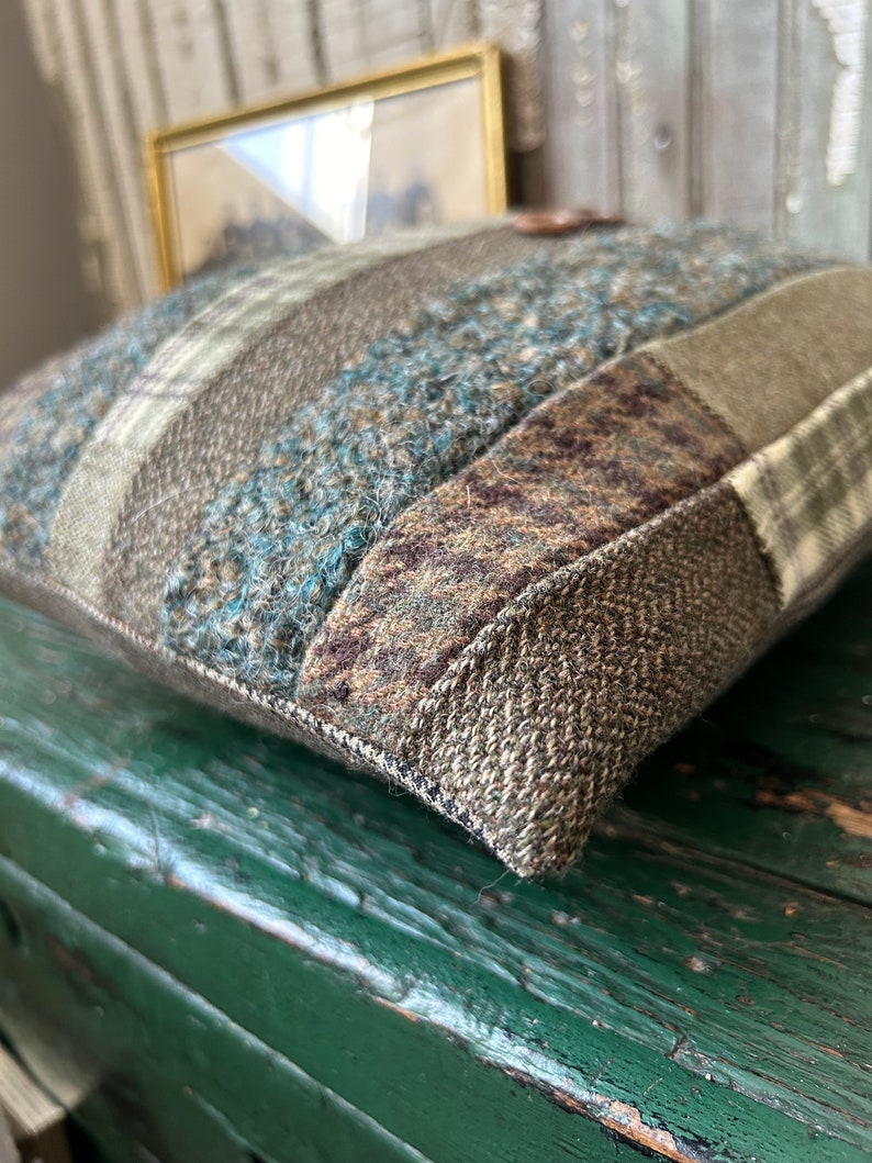 K&ouml;nnte beinhalten: Ein braunes, gr&uuml;nes und blaues Patchwork-Kissen mit Knopfdetail. Das Kissen ist aus einem weichen, strukturierten Stoff gefertigt und hat einen leicht ausgefransten Rand.