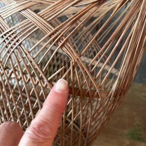 May include: Close-up of a woven wicker basket with a natural brown color. The basket's construction features a complex pattern of interwoven reeds, creating a textured surface. The basket appears to be handmade.