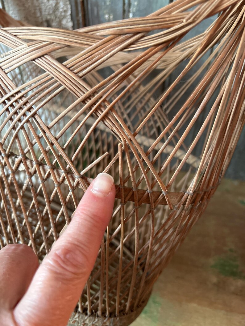 May include: Close-up of a woven wicker basket with a natural brown color. The basket's construction features a complex pattern of interwoven reeds, creating a textured surface. The basket appears to be handmade.