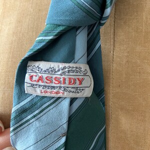Może przedstawiać: Krawat w niebiesko-zielone paski z białą metką z napisem "CASSIDY LONDON".