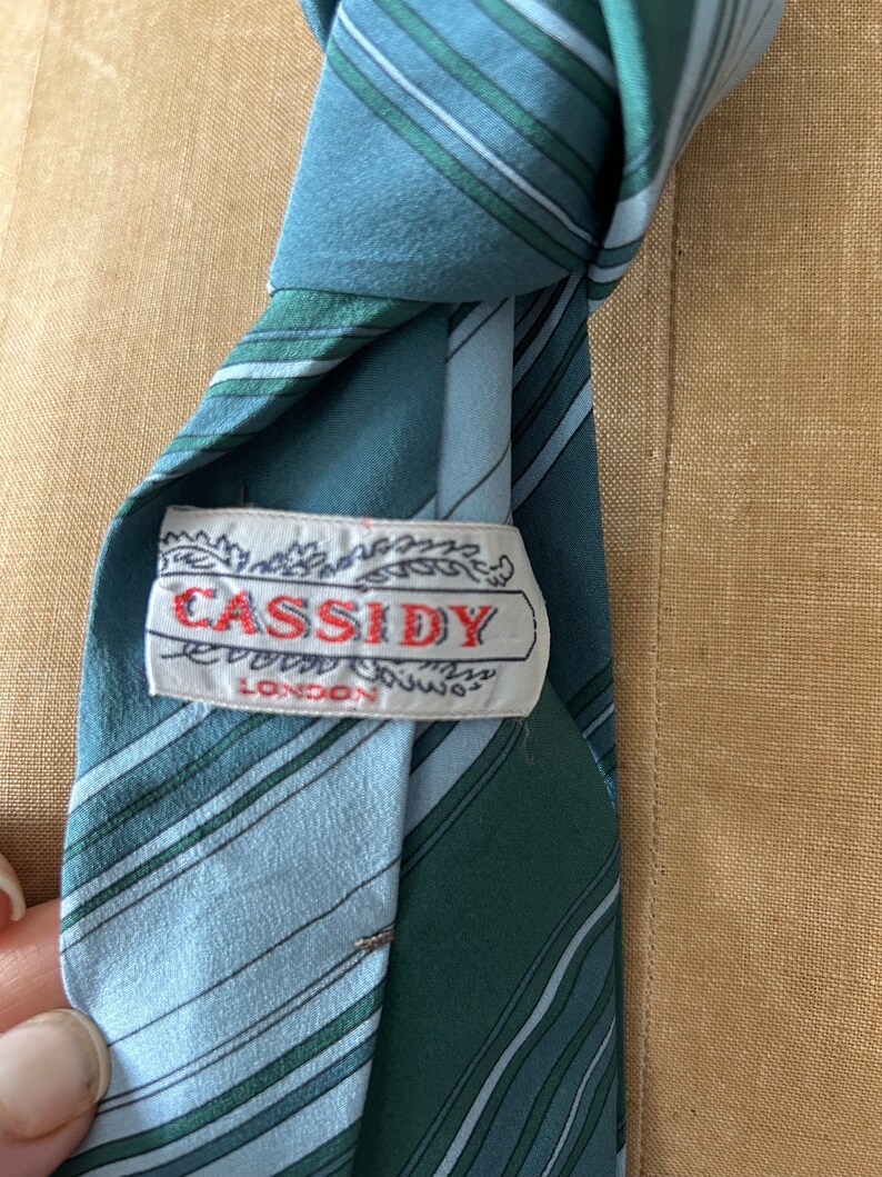 Może przedstawiać: Krawat w niebiesko-zielone paski z białą metką z napisem "CASSIDY LONDON".
