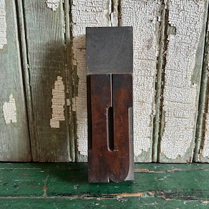 May include: A vintage wooden letterpress block with the letter "U" carved into it. The block is made of dark wood and has a worn, rustic appearance.
