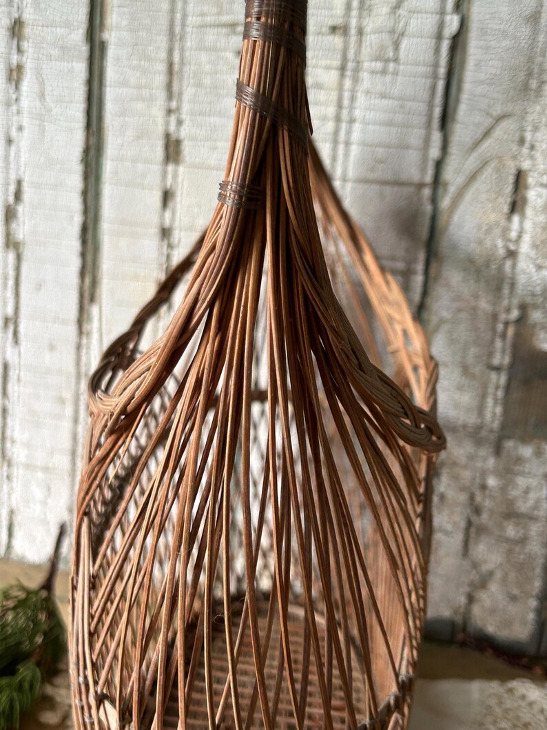 May include: A tall, woven wicker basket with a rounded top and a flared base. The basket is made of light brown wicker and has a natural, rustic appearance. The wicker is tightly woven, creating a sturdy structure. The basket is ideal for storage or decoration.