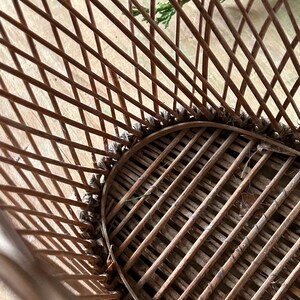 May include: Close-up of a brown wicker chair with a woven seat and back. The chair has a rounded shape and is made of thin, interwoven wooden rods. The chair is designed for outdoor or indoor use.