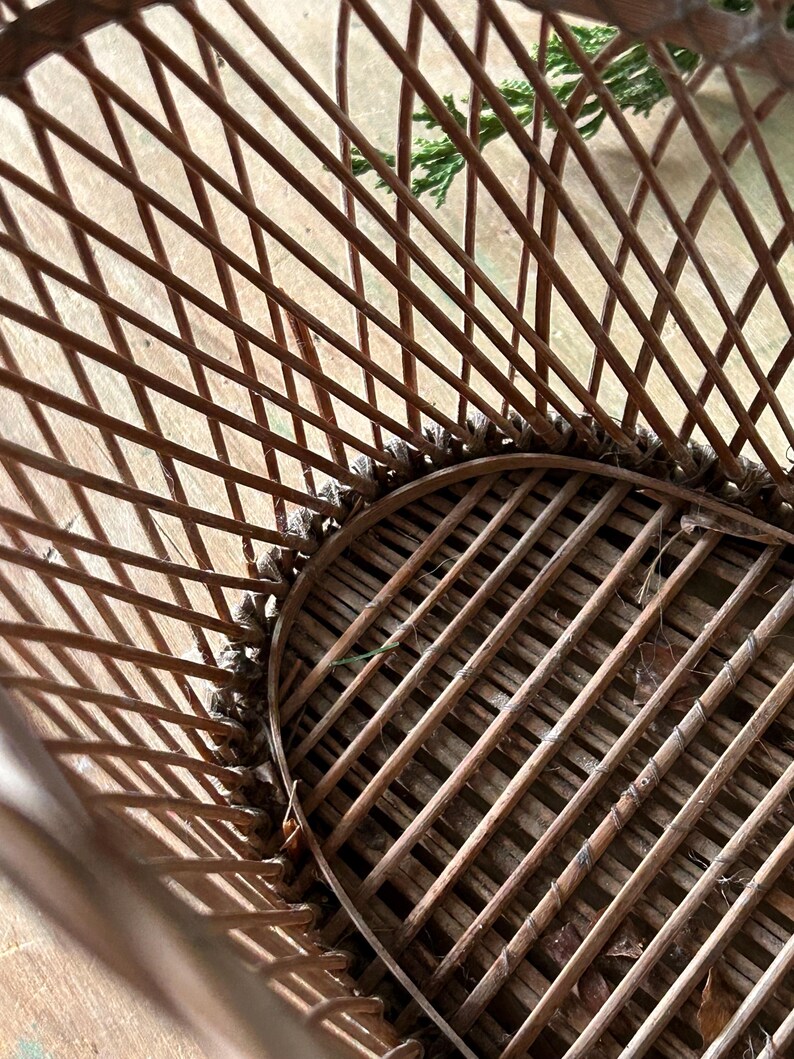 May include: Close-up of a brown wicker chair with a woven seat and back. The chair has a rounded shape and is made of thin, interwoven wooden rods. The chair is designed for outdoor or indoor use.