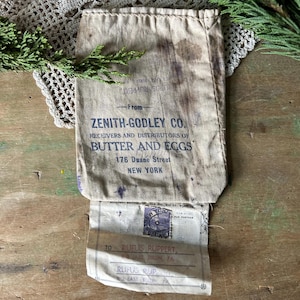 May include: A vintage off-white canvas shipping bag with dark stains and printed text reading Zenith-Godley Co. Receivers and Distributors of Butter and Eggs, 176 Duane Street, New York. An attached shipping label is addressed to Rufus Ruppert.