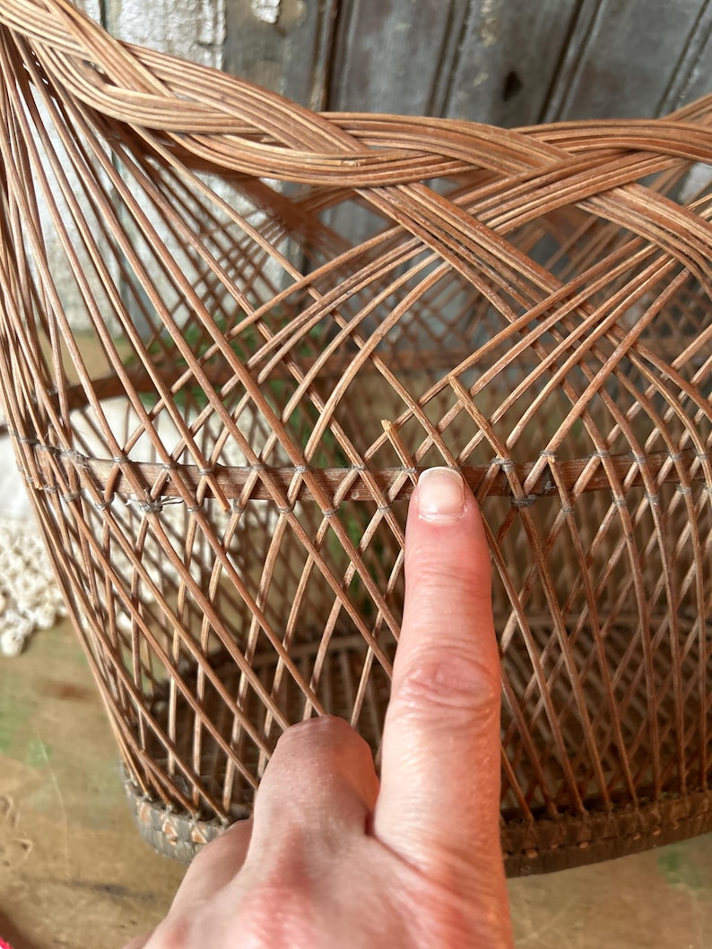 May include: A woven wicker basket with a rounded shape. The basket is made of thin, light brown wicker strips, intricately woven to create a lattice pattern. The base of the basket is reinforced with a darker, thicker material. The basket is empty.