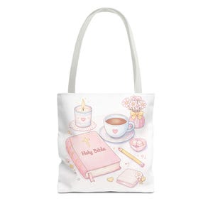 Peut inclure: Sac fourre-tout blanc avec une illustration pastel d'une Sainte Bible rose, d'une tasse de café, d'une bougie allumée et d'un petit vase de fleurs. Les mots "Holy Bible" sont imprimés sur la couverture. Un crayon et des sucres sont également visibles.