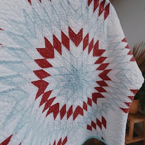 May include: A white quilt with a red and white starburst pattern. The quilt is made of cotton and has a soft, quilted texture.