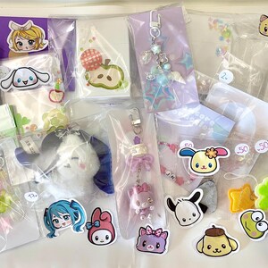 May include: A collection of various character-themed keychains, stickers, and accessories in clear plastic packaging. The items feature cartoon characters in various colors, including Hello Kitty, Cinnamoroll, and My Melody. Some items are adorned with beads and charms.