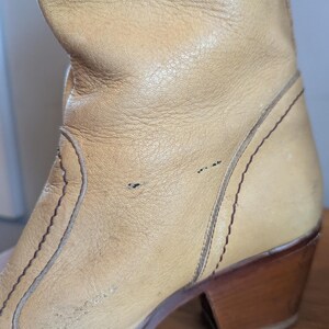 Op de afbeelding: Close-up van een bruinleren laars met een houten hak. De laars heeft decoratieve stiksels en een versleten uiterlijk. De hak is ongeveer 7,6 cm hoog.