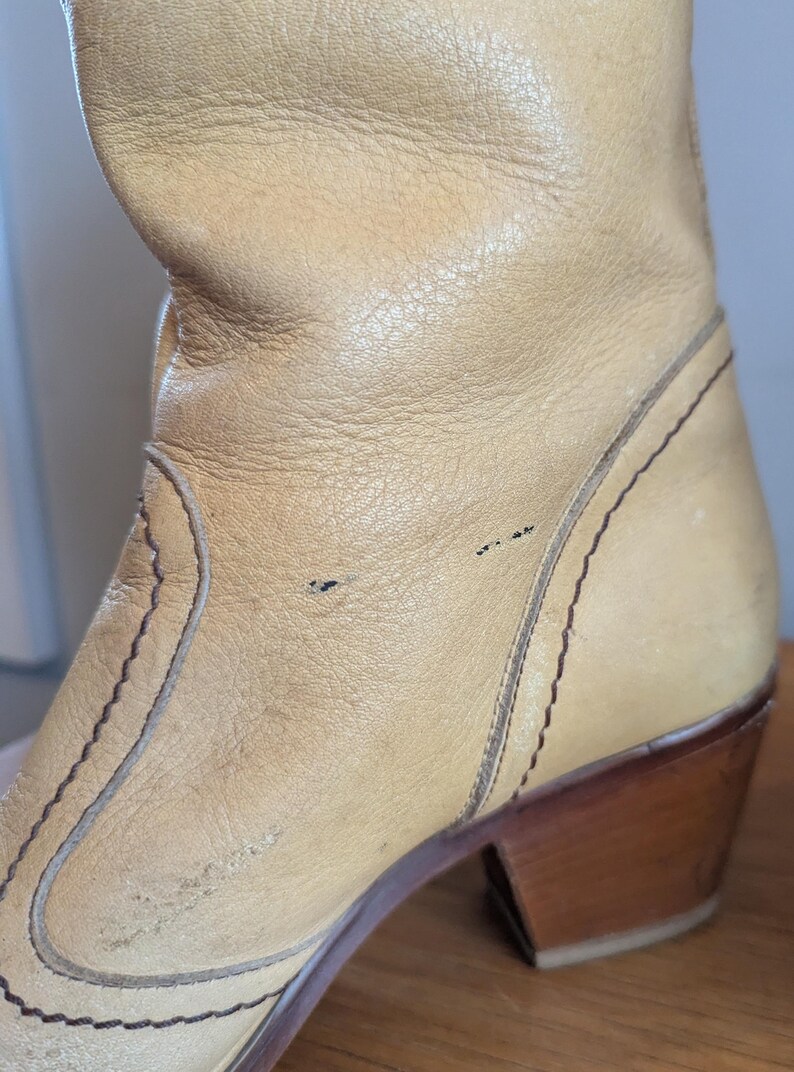 Op de afbeelding: Close-up van een bruinleren laars met een houten hak. De laars heeft decoratieve stiksels en een versleten uiterlijk. De hak is ongeveer 7,6 cm hoog.