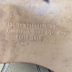 Op de afbeelding: Close-up van een schoenzool met de tekst "MADE IN AUSTRALIA BY J. ROBINS & SONS P/L RESIN SOLE". De zool is lichtbruin van kleur en vertoont slijtage.