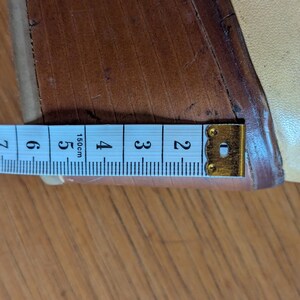 Op de afbeelding: Een close-up toont een beige schoen met een houten sleehak. Een meetlint is naast de hak geplaatst, met een meting van ongeveer 5 cm.