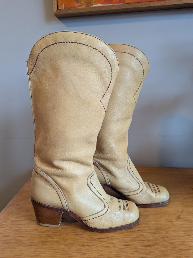 Op de afbeelding: Een paar bruinleren cowboylaarzen met een blokhak. De laarzen hebben decoratieve stiksels en een ronde neus. De laarzen zijn kniehoog en hebben een klassiek Western-ontwerp.