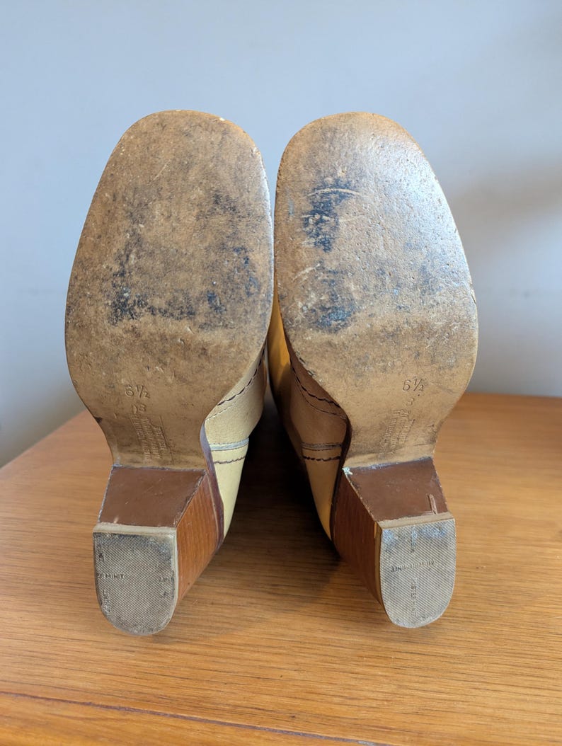 Op de afbeelding: Een paar vintage beige leren laarzen, maat 37, met houten blokhakken. De zolen vertonen slijtage. De laarzen staan op een houten oppervlak.