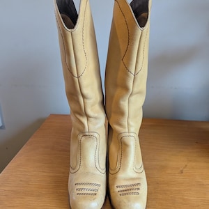 Op de afbeelding: Een paar lichtbruine leren cowboylaarzen. De laarzen hebben een hoge schacht, een ronde neus en een blokhak. De laarzen zijn versierd met gestikte details in een donkerdere bruine draad. De laarzen zijn ongeveer 35,5 cm hoog.