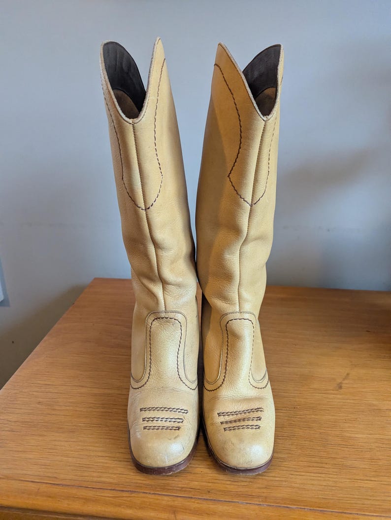 Op de afbeelding: Een paar lichtbruine leren cowboylaarzen. De laarzen hebben een hoge schacht, een ronde neus en een blokhak. De laarzen zijn versierd met gestikte details in een donkerdere bruine draad. De laarzen zijn ongeveer 35,5 cm hoog.