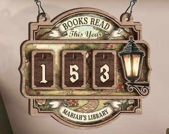 Może przedstawiać: Drewniany znak z napisem "BOOKS READ This Year" i "MARIAH'S LIBRARY". Znak ma trzy wyświetlacze numeryczne pokazujące "153". Ozdobna latarnia znajduje się po prawej stronie znaku. Znak wisi na łańcuchu.