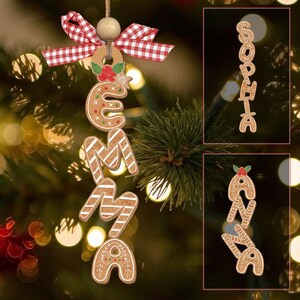 Puede incluir: Adorno navideño estilo pan de jengibre que deletrea "EMMA", con un lazo de cuadros rojos y blancos y una cuenta de madera. Las letras están decoradas con glaseado blanco y detalles festivos. Adornos adicionales que deletrean "SOPHIA" y "AVA".