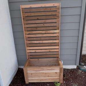 Puede incluir: Una jardinera rectangular de madera con un panel trasero de enrejado vertical alto e integrado. La estructura est&aacute; construida con tablones de madera de color marr&oacute;n claro natural con listones horizontales y una base profunda.