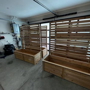 May include: Wooden rectangular planters and matching slatted privacy screens. The planters are made of light-colored wood and are placed in front of the screens. The screens are made of horizontal wooden slats.