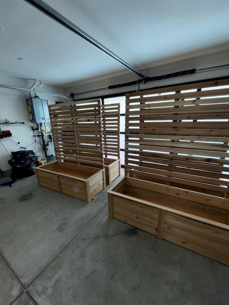 May include: Wooden rectangular planters and matching slatted privacy screens. The planters are made of light-colored wood and are placed in front of the screens. The screens are made of horizontal wooden slats.