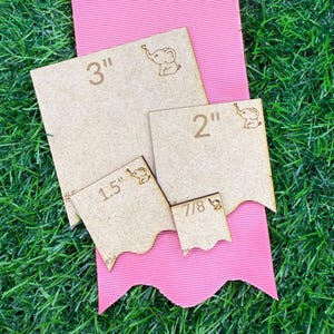 May include: A collection of wooden craft pieces in various sizes, including 3", 2", 1.5", and 7/8", each with an engraved elephant design. The pieces are arranged on a pink ribbon against a backdrop of green grass.