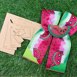 May include: A watermelon-themed hair bow with a glittery watermelon slice embellishment. The bow features a red, pink, and green watermelon pattern. Next to the bow are several brown cardboard templates with the text "BettyGirlyBows".