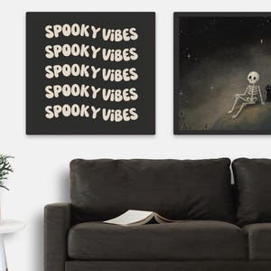 Puede incluir: Dos impresiones art&iacute;sticas enmarcadas con tem&aacute;tica de Halloween. Una presenta el texto "Spooky Vibes" repetido sobre un fondo negro. La otra representa un esqueleto y un gato negro bajo un cielo estrellado.