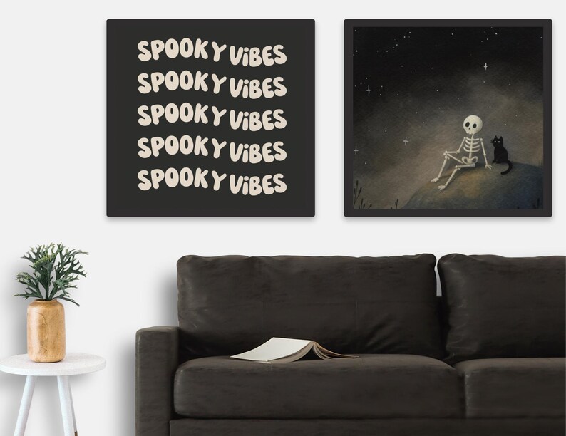 Puede incluir: Dos impresiones art&iacute;sticas enmarcadas con tem&aacute;tica de Halloween. Una presenta el texto "Spooky Vibes" repetido sobre un fondo negro. La otra representa un esqueleto y un gato negro bajo un cielo estrellado.