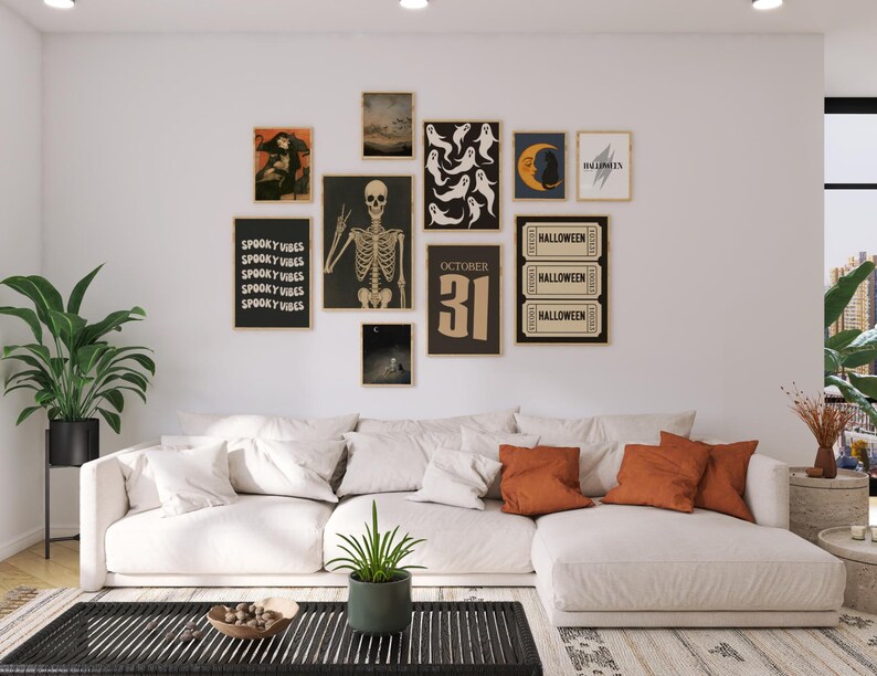 Puede incluir: Un sal&oacute;n decorado para Halloween con arte enmarcado. El arte incluye un esqueleto, fantasmas, una luna y el texto "October 31". Debajo del arte hay un sof&aacute; seccional blanco con cojines naranjas.
