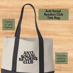 May include: Cream-colored tote bag with black handles and base. The words "ANTI SOCIAL READERS CLUB" are printed in black on the front. The bag has an exterior pocket and the option to add a name.