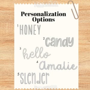 May include: A white paper with the text "Personalization Options" and five examples of personalized text: "HONEY", "candy", "hello", "Amalie", and "SLENDER". A paperclip is attached to the top right corner.