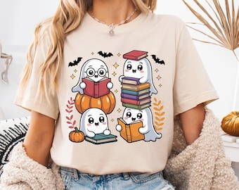 Op de afbeelding: Beige T-shirt met een cartoonontwerp van vier geesten die boeken lezen. De geesten zitten op pompoenen en boeken, met vleermuizen en herfstbladeren. Er is ook een kleine pompoen aanwezig. Het shirt is een comfortabele, casual stijl.