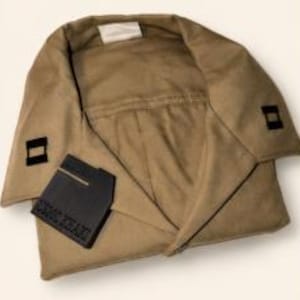 May include: A tan-colored, folded garment with a rectangular black patch and a smaller black square on each side. The patch has white text. The garment appears to be made of a soft, possibly suede-like material.