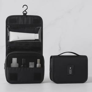 K&ouml;nnte beinhalten: Schwarzes Reise-Kulturbeutel-Set. Eine Tasche ist ein h&auml;ngender Organizer mit transparenten Taschen und einem Netzfach. Die andere ist eine kleine, rechteckige Tasche mit Griff und einem Reise-Logo.