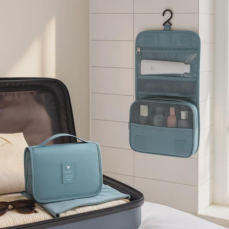 K&ouml;nnte beinhalten: Eine tealfarbene Reise-Kulturtasche mit Griff liegt in einem offenen Koffer. Ein passender h&auml;ngender Kulturbeutel h&auml;ngt an einem Haken an der Wand. Der Organizer hat mehrere F&auml;cher und enth&auml;lt verschiedene Toilettenartikel.
