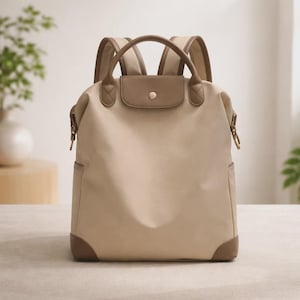 Puede incluir: Mochila beige con detalles en cuero marrón. Cuenta con un asa superior, correas ajustables y cierre de solapa con botón. Las esquinas inferiores y la solapa son marrones. Tiene dos bolsillos laterales.