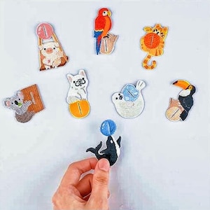 Puede incluir: Colección de parches bordados de animales, incluyendo un cerdo, un loro, un tigre, un koala, un perro, una foca, un tucán y una orca. Cada parche presenta colores vibrantes y costuras detalladas, ideal para añadir a ropa o accesorios.