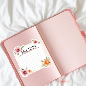 May include: Open pink journal with a floral sticker that reads "Bible Notes." The sticker has a white background with lines for writing and is decorated with watercolor flowers in shades of pink, orange, and yellow.