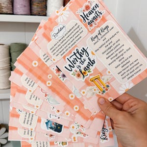May include: A stack of rectangular cards with a light pink and white checkered background, decorated with white daisy illustrations. The cards feature religious text including "Worthy is the Lamb," "Heaven awaits," and "King of Kings," alongside floral accents and gold pillar graphics.